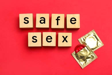Words SAFE SEX made with wooden cubes and shiny condoms on red background, flat lay