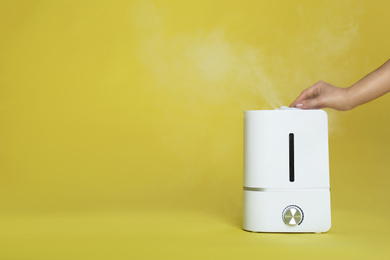 Woman using modern air humidifier on yellow background, closeup. Space for text
