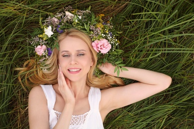 Young woman wearing wreath made of beautiful flowers on green grass, top view