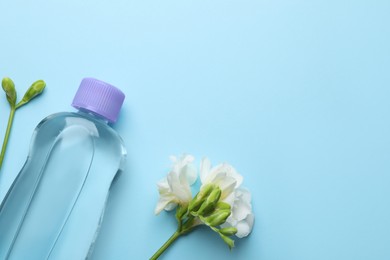 Photo of Bottle of baby oil and freesia flowers on light blue background, flat lay. Space for text