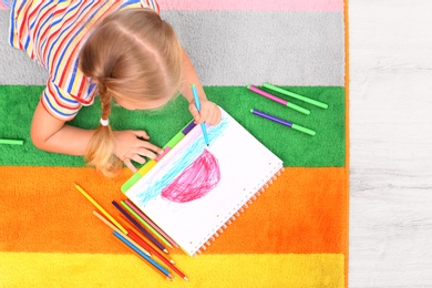 Little left-handed girl drawing on floor in room, above view