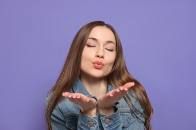 Photo of Beautiful young woman blowing kiss on purple background