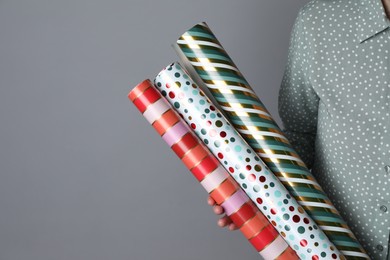Photo of Woman holding different colorful wrapping paper rolls on grey background, closeup. Space for text