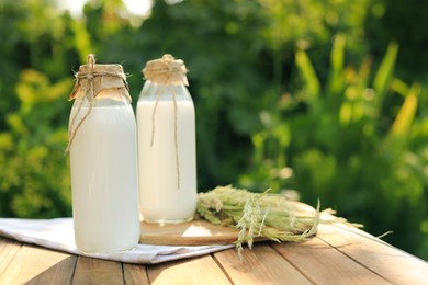 Bottles of tasty fresh milk on wooden table outdoors, space for text