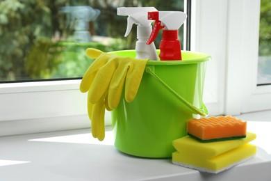 Green bucket with cleaning supplies and tools on window sill indoors