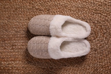 Photo of Pair of warm stylish slippers on wicker carpet, top view