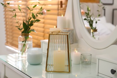 Burning scented candles and bouquet on dressing table indoors