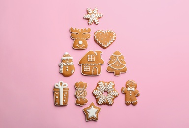 Photo of Delicious gingerbread cookies arranged in shape of Christmas tree on pink background, flat lay