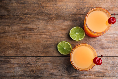 Fresh alcoholic Tequila Sunrise cocktails on wooden table, flat lay. Space for text