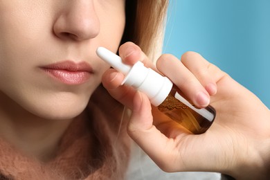 Sick young woman using nasal spray on light blue background, closeup