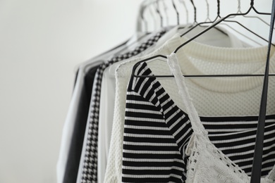 Rack with stylish clothes near white wall, closeup