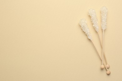 Wooden sticks with sugar crystals and space for text on beige background, flat lay. Tasty rock candies