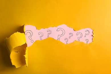 Question marks on pink background, view through hole in yellow paper