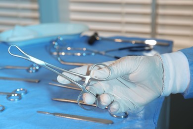 Doctor holding medical clamps near table with different surgical instruments indoors, closeup