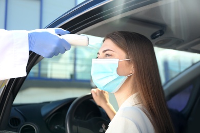Doctor measuring woman's temperature with non contact infrared thermometer in car
