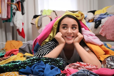 Happy young woman with lots of clothes on floor in room. Fast fashion
