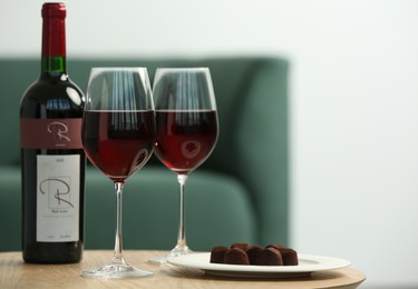 Bottle and glasses of red wine with chocolate candies on wooden table in living room