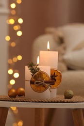Photo of Beautiful burning candles decorated with dry orange slices and cinnamon sticks on white table indoors. Christmas atmosphere
