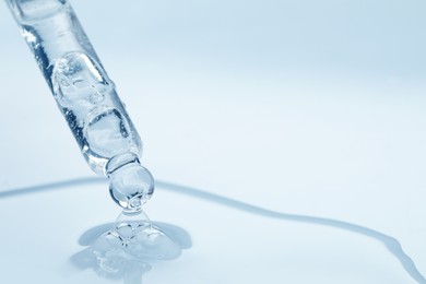 Dripping face serum from pipette on white background, closeup. Space for text