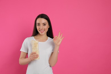 Photo of Happy young woman with tasty shawarma showing okay gesture on pink background. Space for text