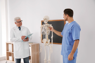 Medical student and professor studying human skeleton anatomy in classroom