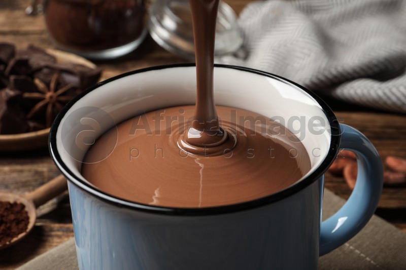 Pouring yummy hot chocolate into mug on table, closeup