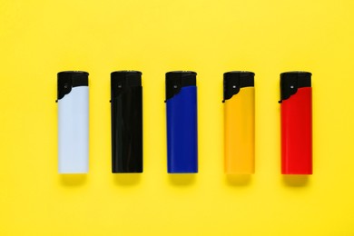 Photo of Stylish small pocket lighters on yellow background, flat lay
