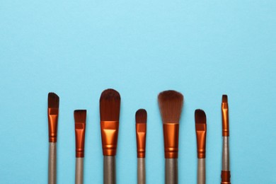 Set of makeup brushes on light blue background, flat lay. Space for text