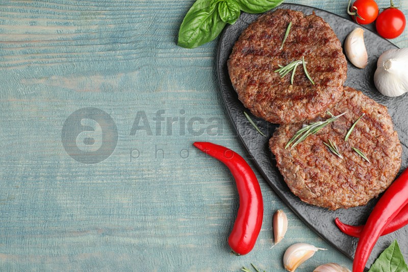 Flat lay composition with grilled meat cutlets for burger on blue wooden table. Space for text