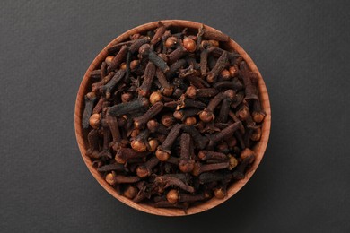 Aromatic dry cloves in wooden bowl on grey background, top view