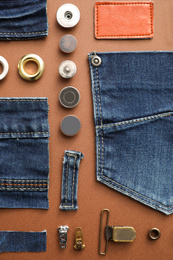Flat lay composition with garment accessories and cutting details for jeans on brown background