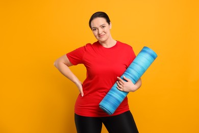 Happy overweight woman with yoga mat on orange background