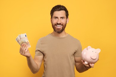 Happy man with money and ceramic piggy bank on orange background