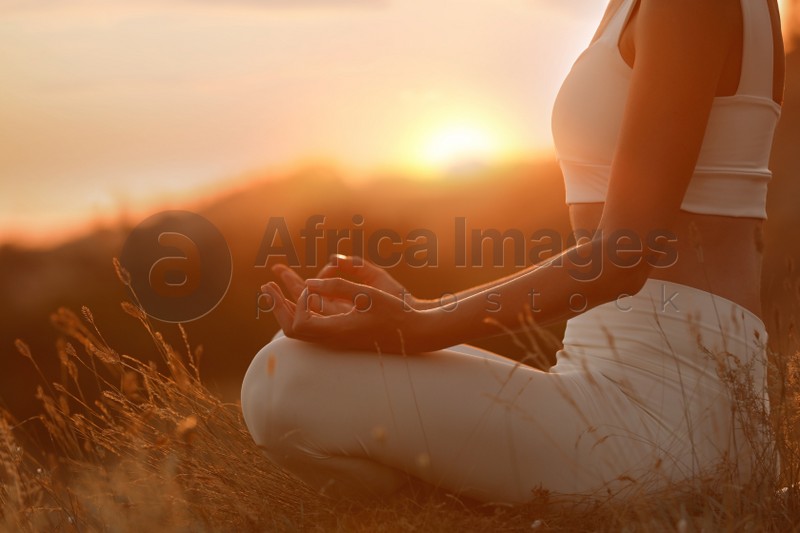 Woman meditating outdoors at sunset, closeup view