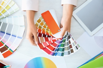 Woman with paint color palette samples and tablet at table, top view