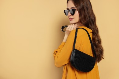 Photo of Beautiful young woman in fashionable outfit with stylish bag on beige background, space for text