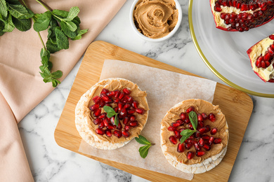 Puffed rice cakes with peanut butter, pomegranate seeds and mint on white marble table, flat lay