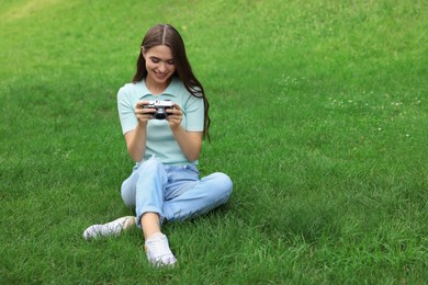 Photo of Young woman with camera on green grass outdoors, space for text. Interesting hobby