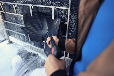 Man cleaning auto mats with high pressure water jet at self-service car wash, closeup