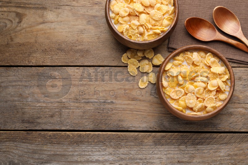 Tasty cornflakes with milk in bowls on wooden table, flat lay. Space for text