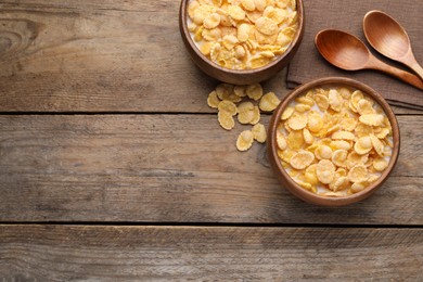 Tasty cornflakes with milk in bowls on wooden table, flat lay. Space for text