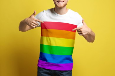 Young man wearing t-shirt with image of LGBT pride flag on yellow background