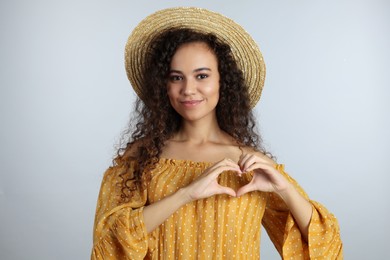 Photo of Happy young African-American woman making heart with hands on light grey background