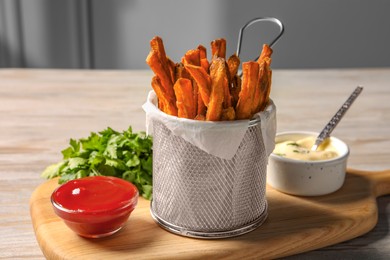 Frying basket with sweet potato fries, sauces and parsley on table