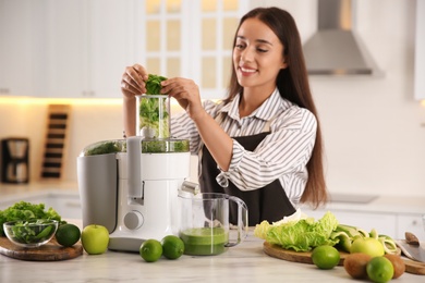 Young woman making tasty fresh juice at table in kitchen
