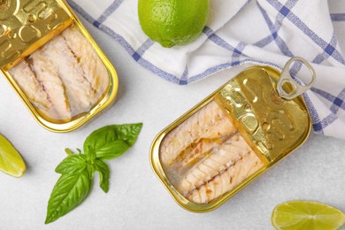 Photo of Open tin cans with mackerel fillets, lime and basil on grey table, flat lay