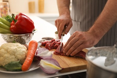 Man cutting meat to make bouillon in kitchen, closeup. Homemade recipe
