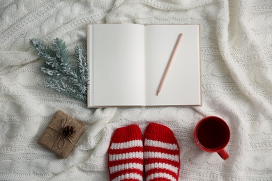 Woman with cup of hot winter drink and notebook on knitted plaid, top view. Cozy season