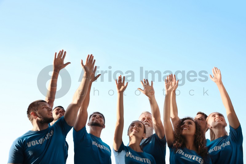Group of volunteers raising hands outdoors on sunny day