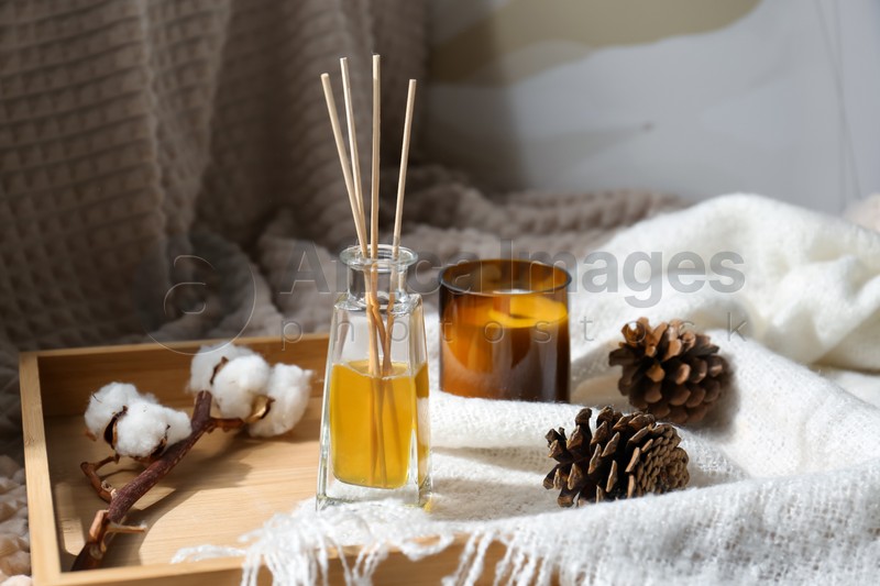 Reed air freshener, candle and pine cones on wooden tray indoors